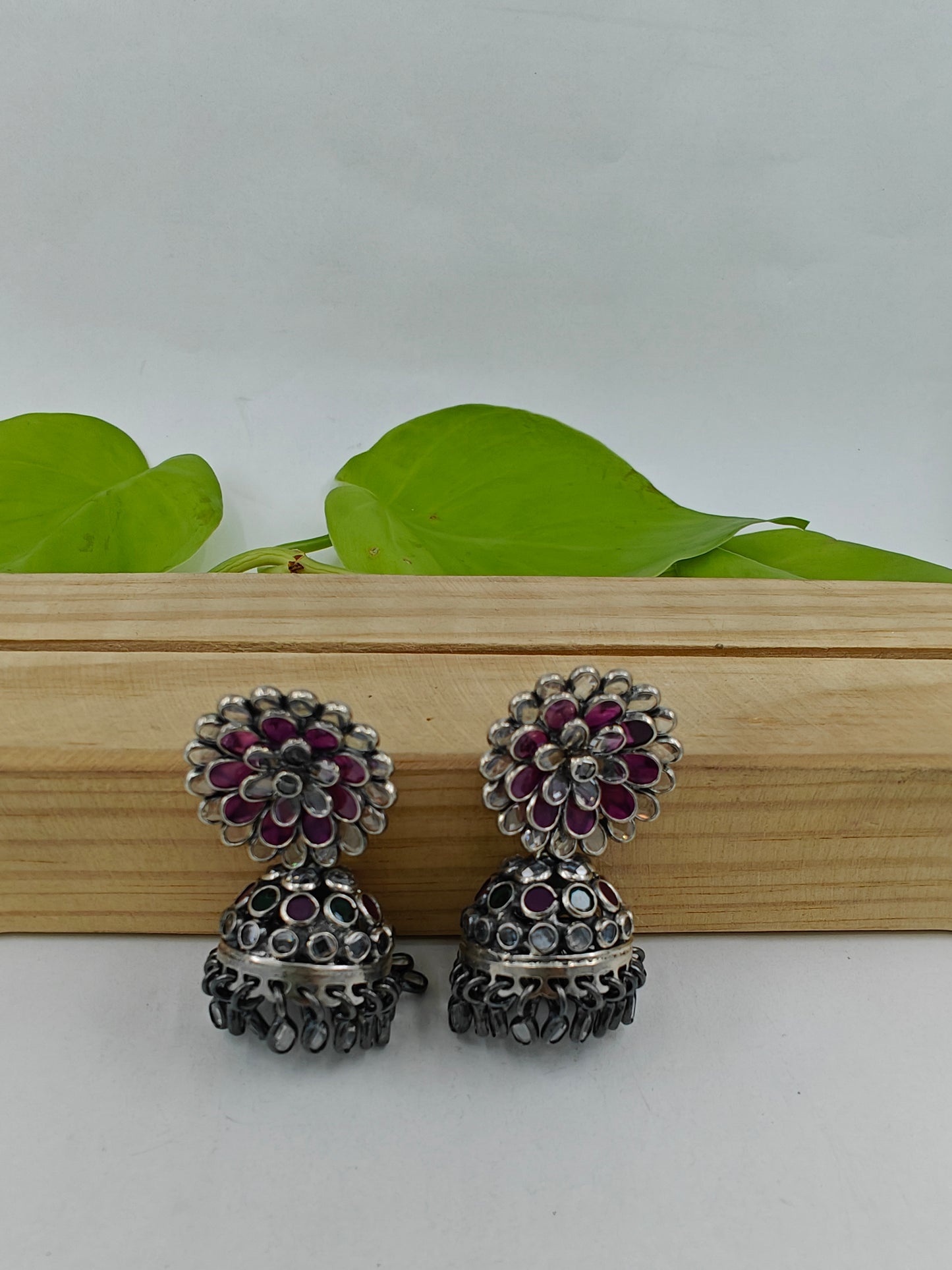 Silver jhumkis (earrings) with red and clear stone petals on a open flower stud