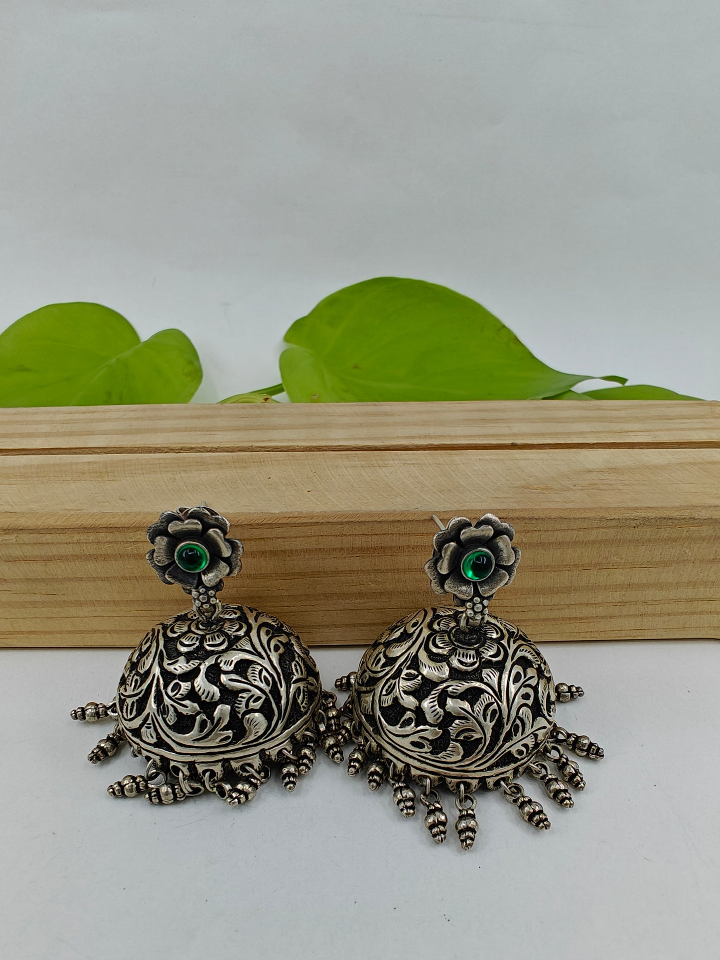 Silver jhumkas (earrings) on a flower stud with green stone