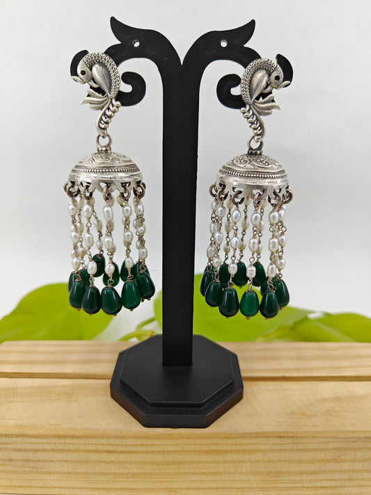 Silver jhumkas (earrings) with pearl and emerald stone hanging on peacock stud