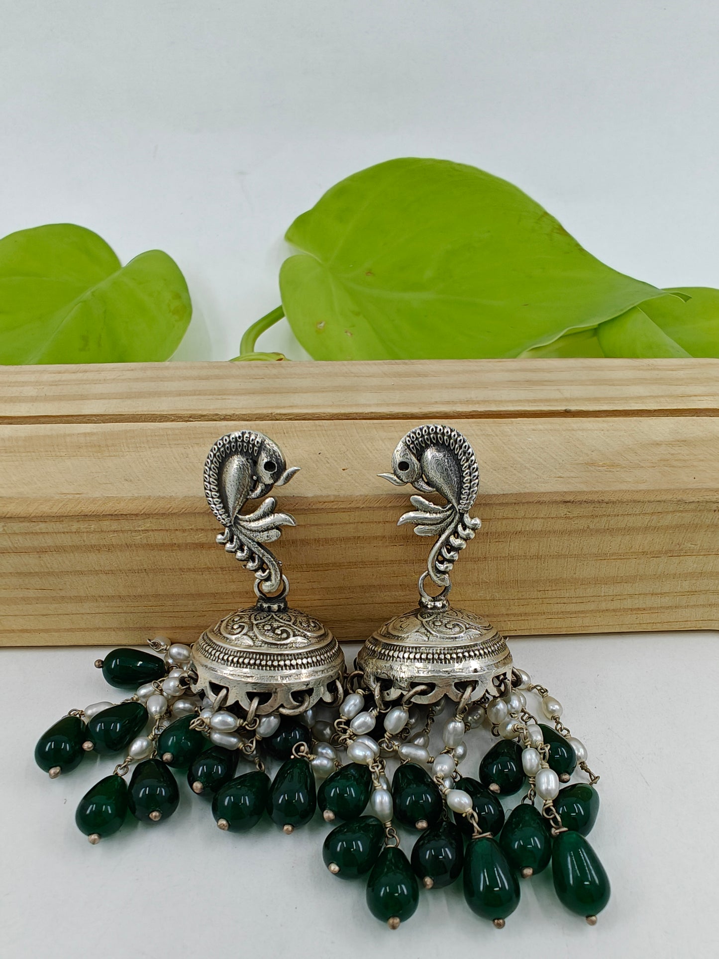 Silver jhumkas (earrings) with pearl and emerald stone hanging on peacock stud