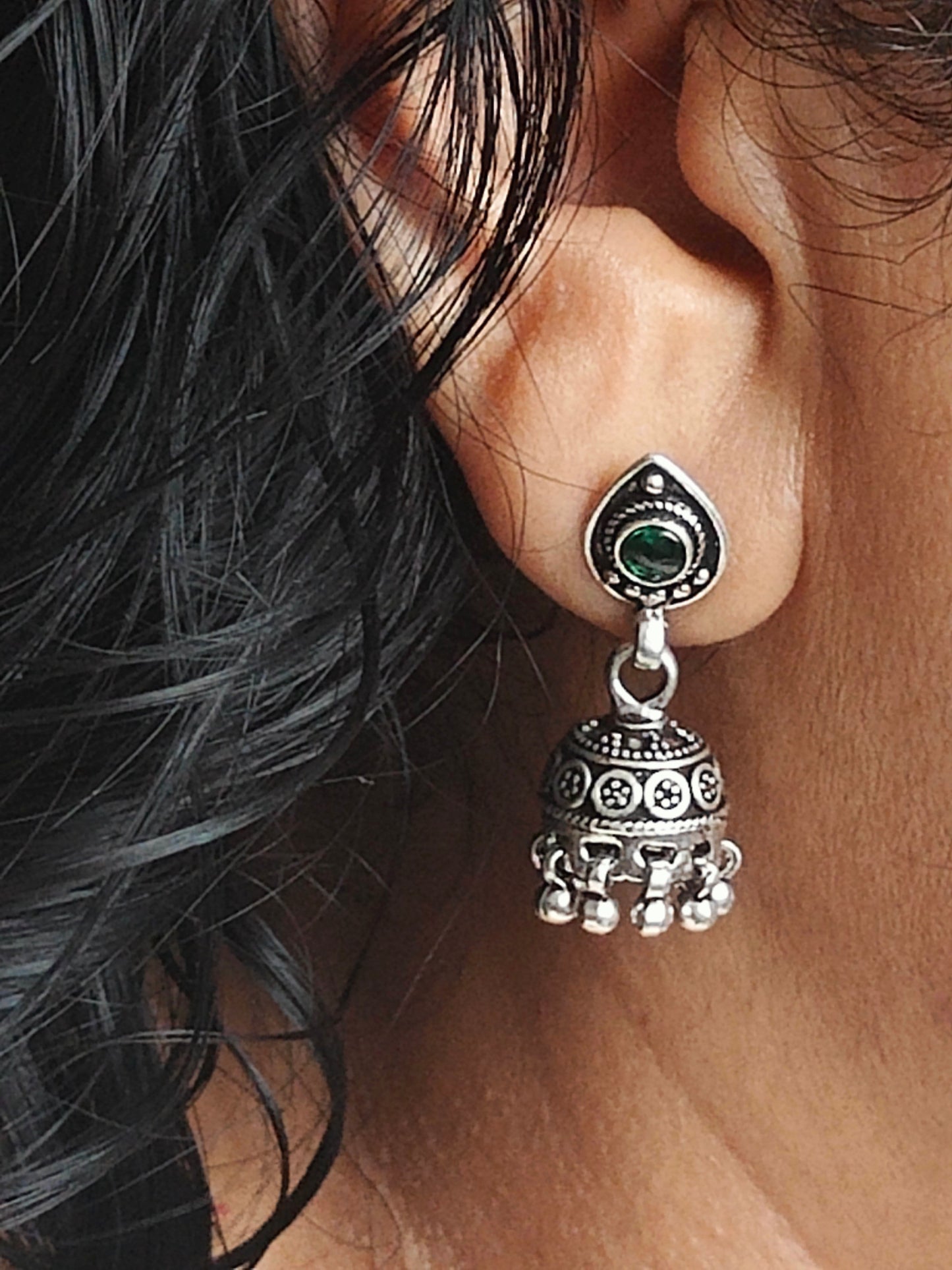 Silver jhumkis (earrings) on a stud with emerald green stone