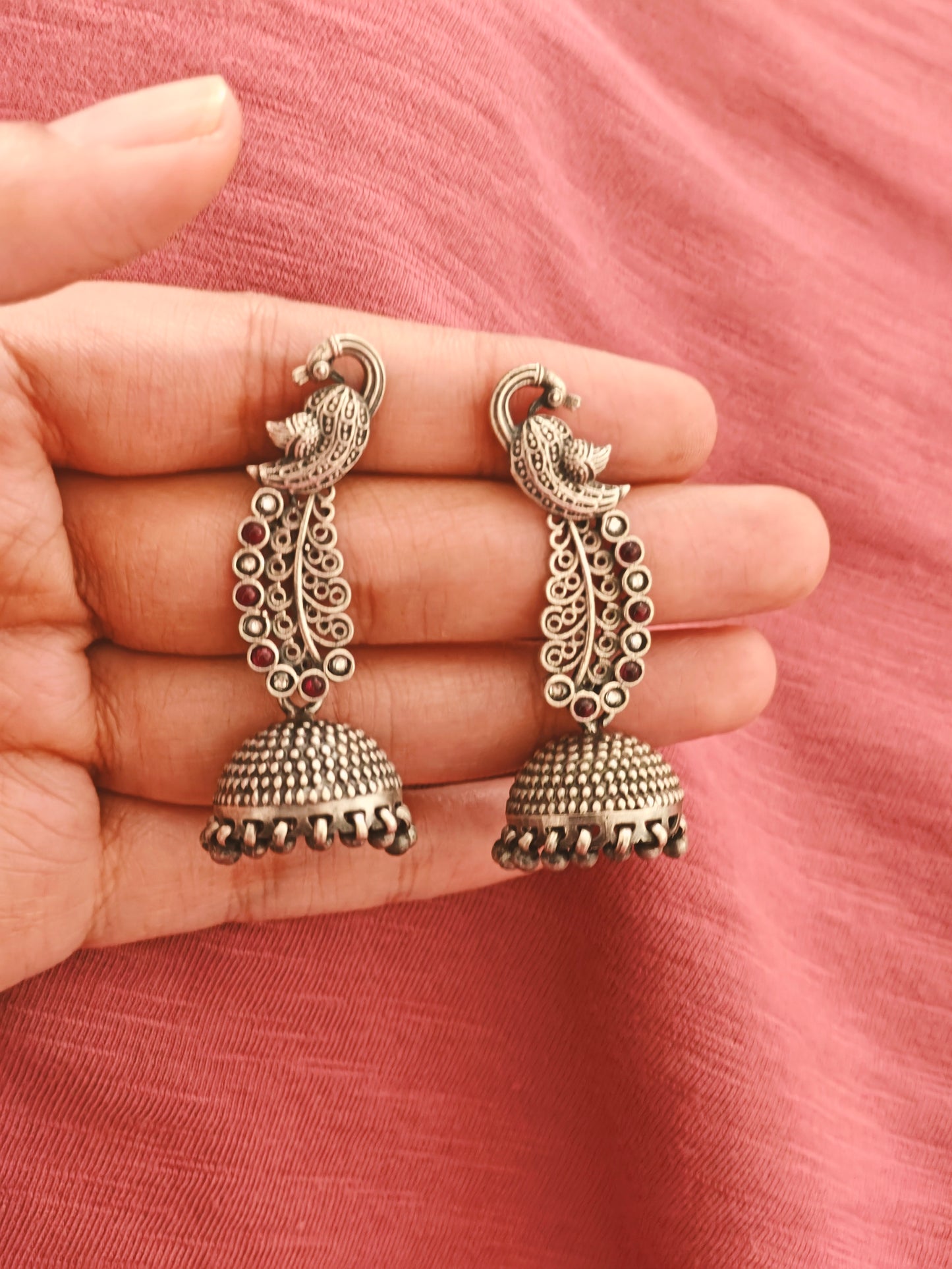 Silver jhumkis (earrings) on peacock studs with long carved feathers