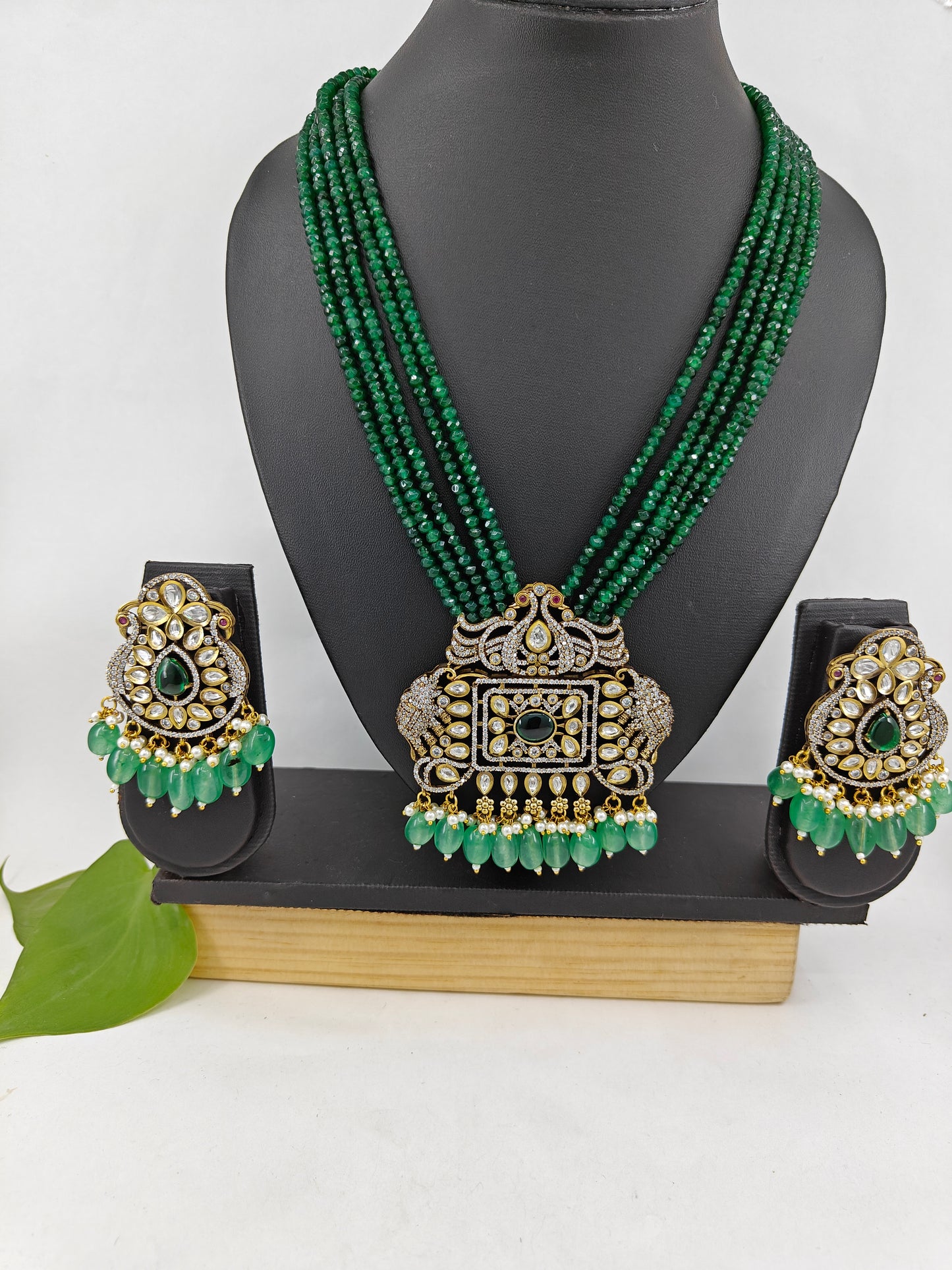 Set in antique gold finish with an elephant and peacock motif pendant in Kundan,CZ and emerald green stones on green strands