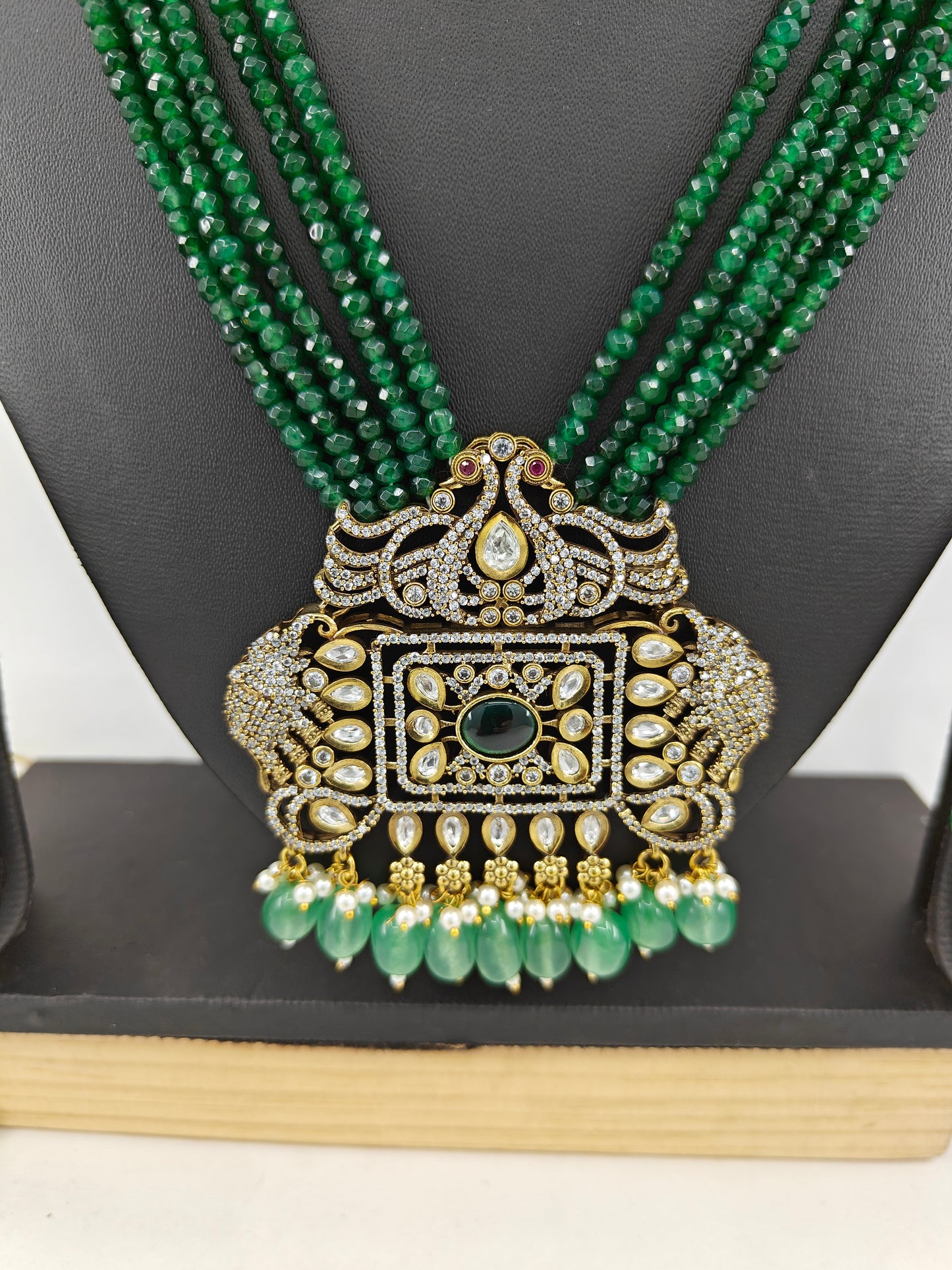 Set in antique gold finish with an elephant and peacock motif pendant in Kundan,CZ and emerald green stones on green strands