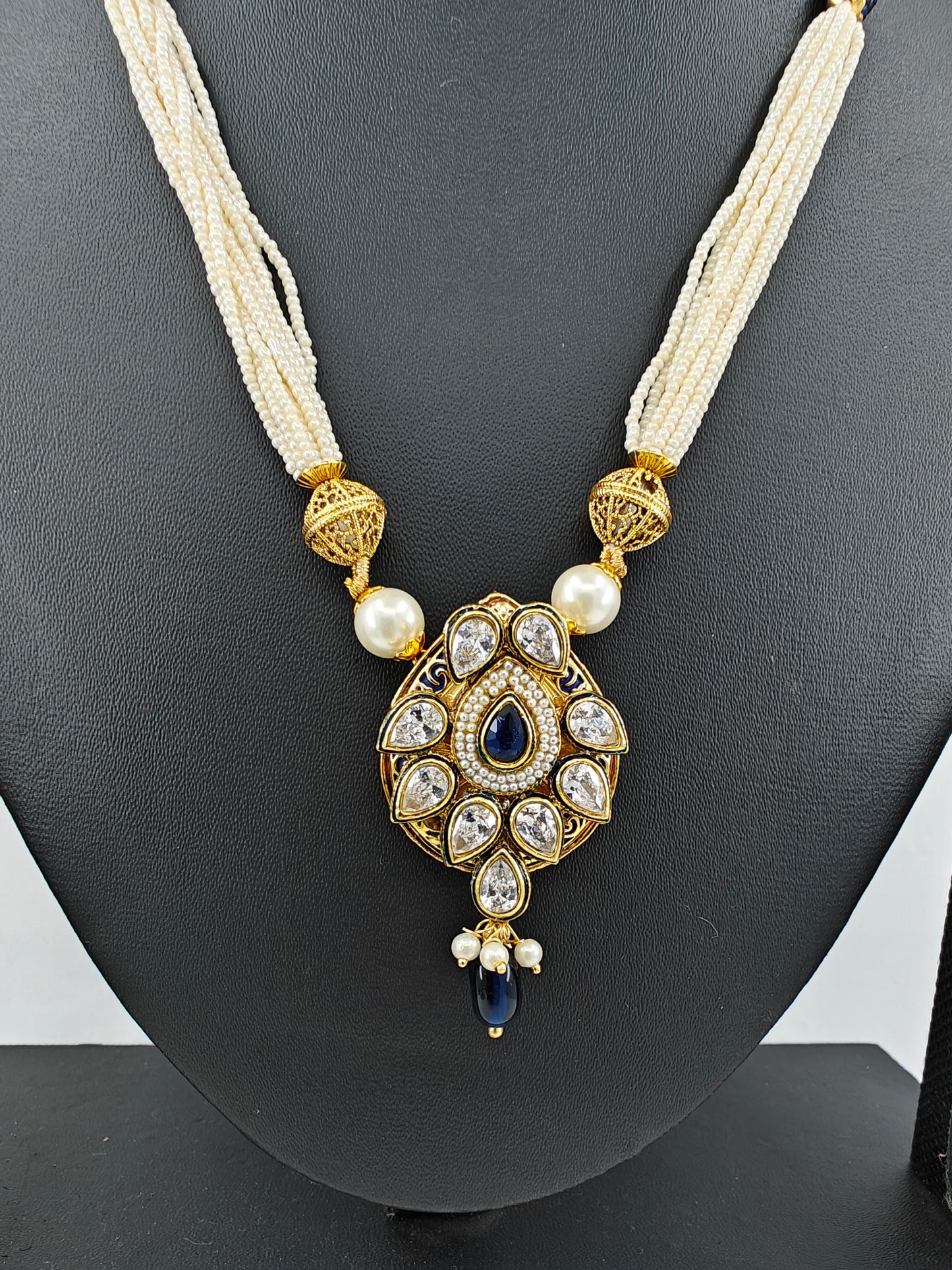 Set in gold finish with kundan, sapphire blue stone on tear drop shaped pendant on poth pearl string.