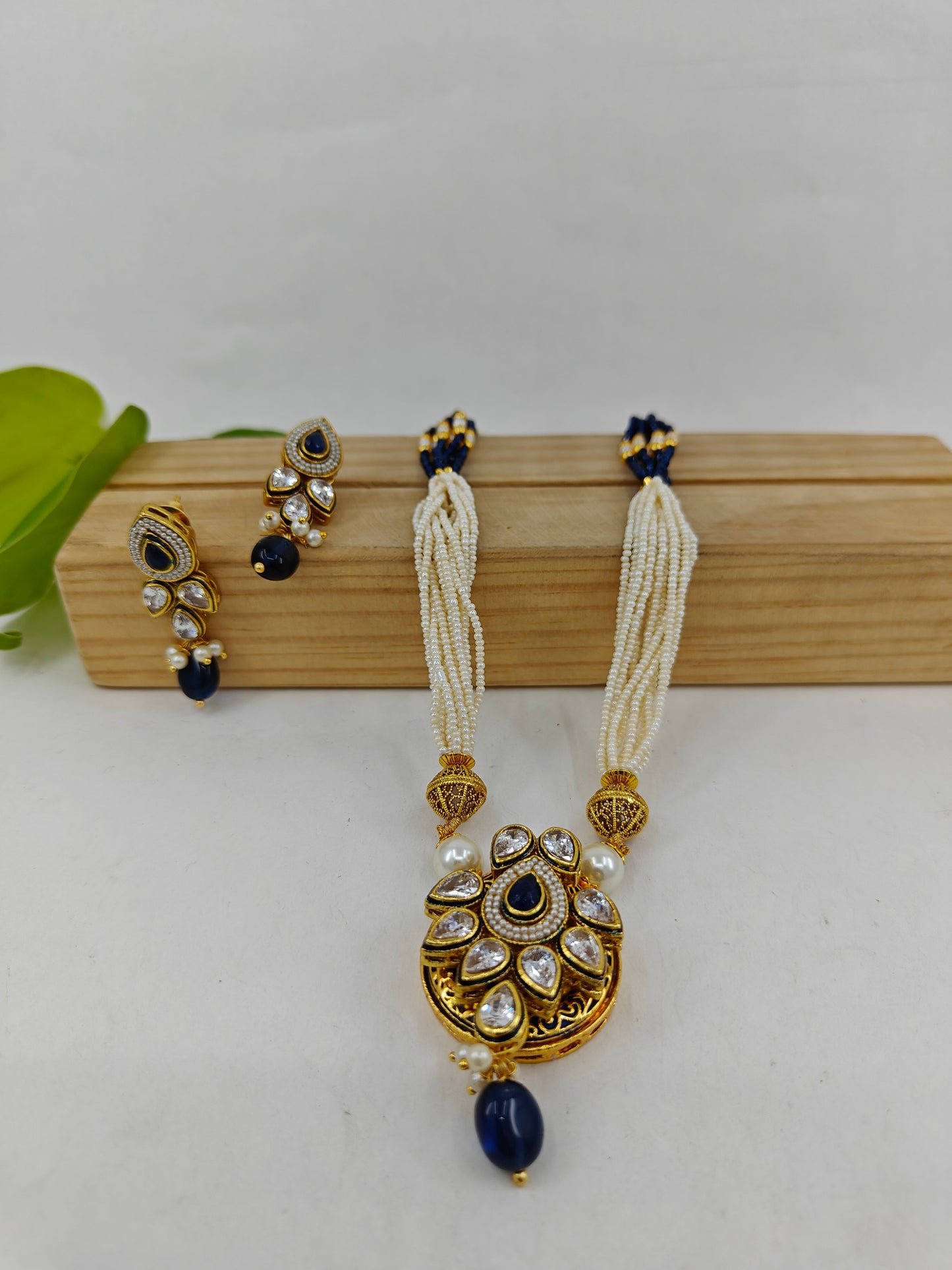 Set in gold finish with kundan, sapphire blue stone on tear drop shaped pendant on poth pearl string.