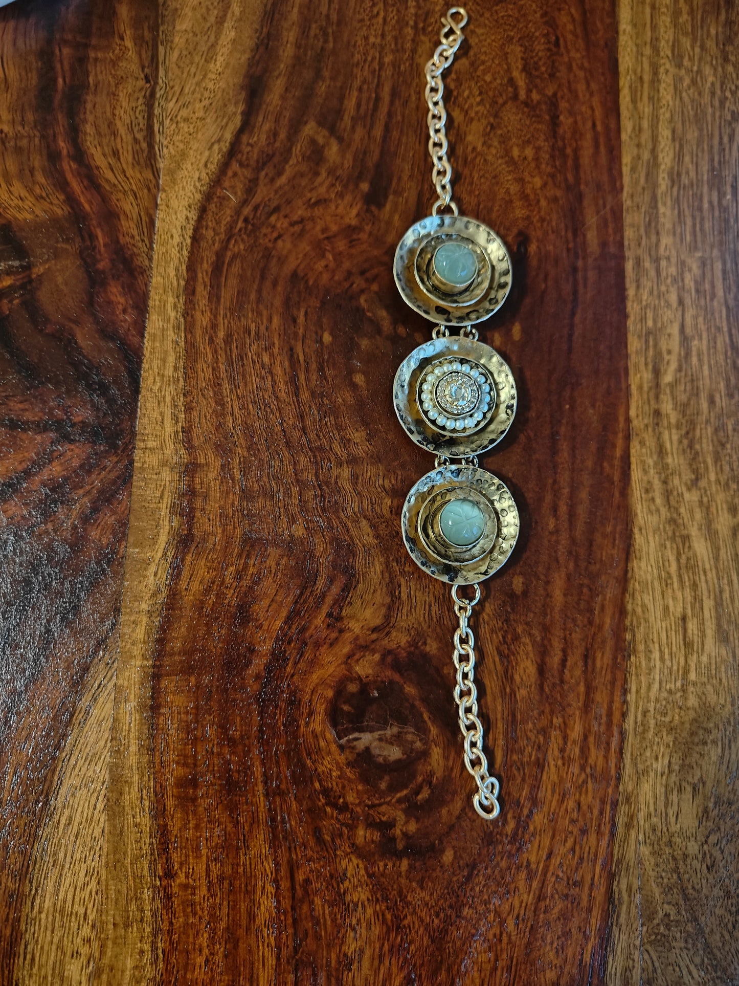 A unique bracelet in beaten plate design with green stone in two kundan and pearls in one