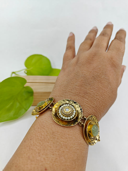 A unique bracelet in beaten plate design with green stone in two kundan and pearls in one