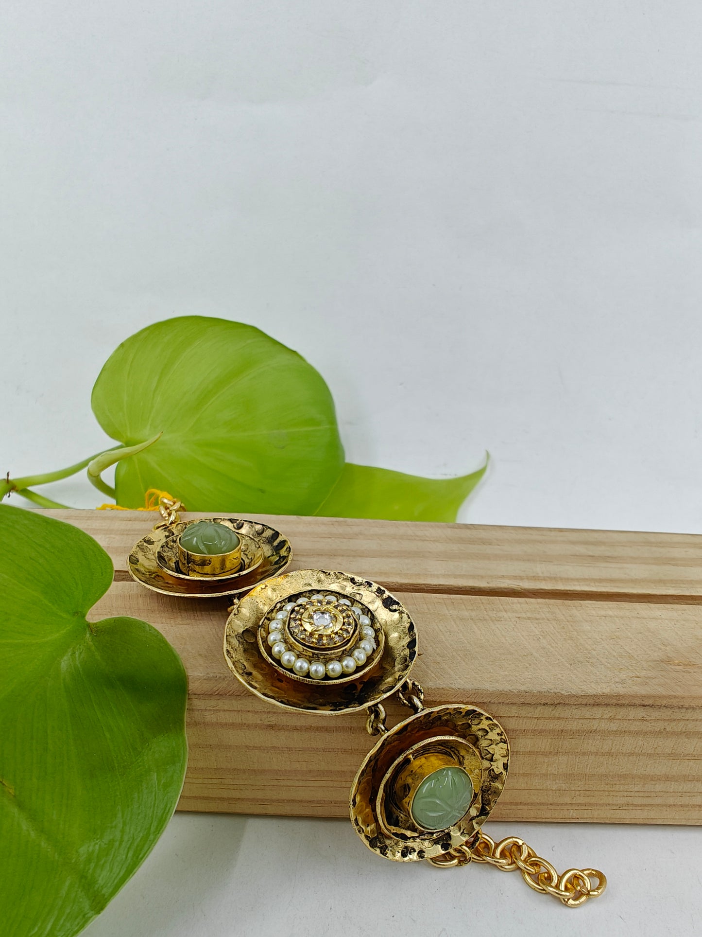 A unique bracelet in beaten plate design with green stone in two kundan and pearls in one