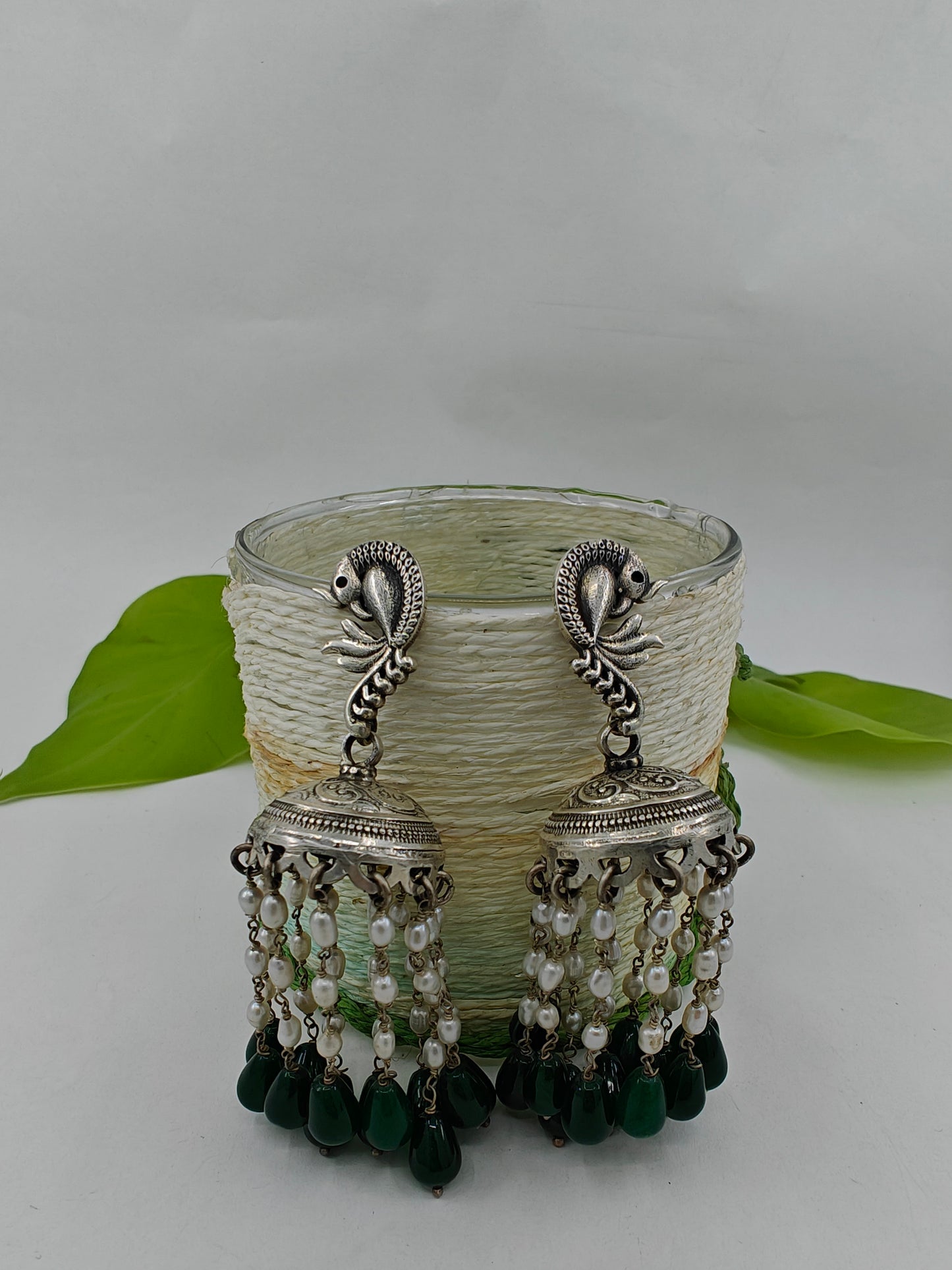 Silver jhumkas (earrings) with pearl and emerald stone hanging on peacock stud