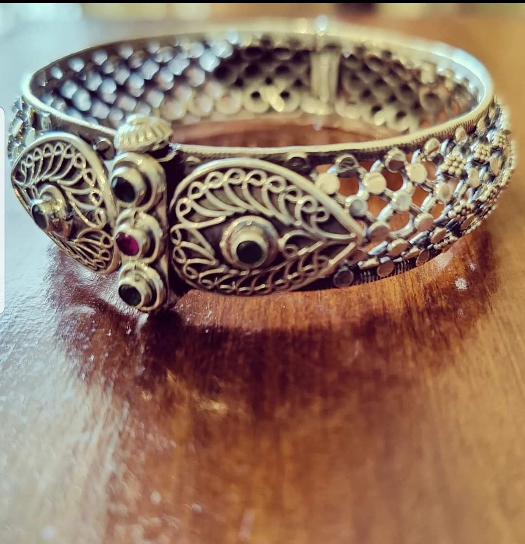 Silver kada (bangle) with intricate jaali (mesh) design enhanced with red and green stone