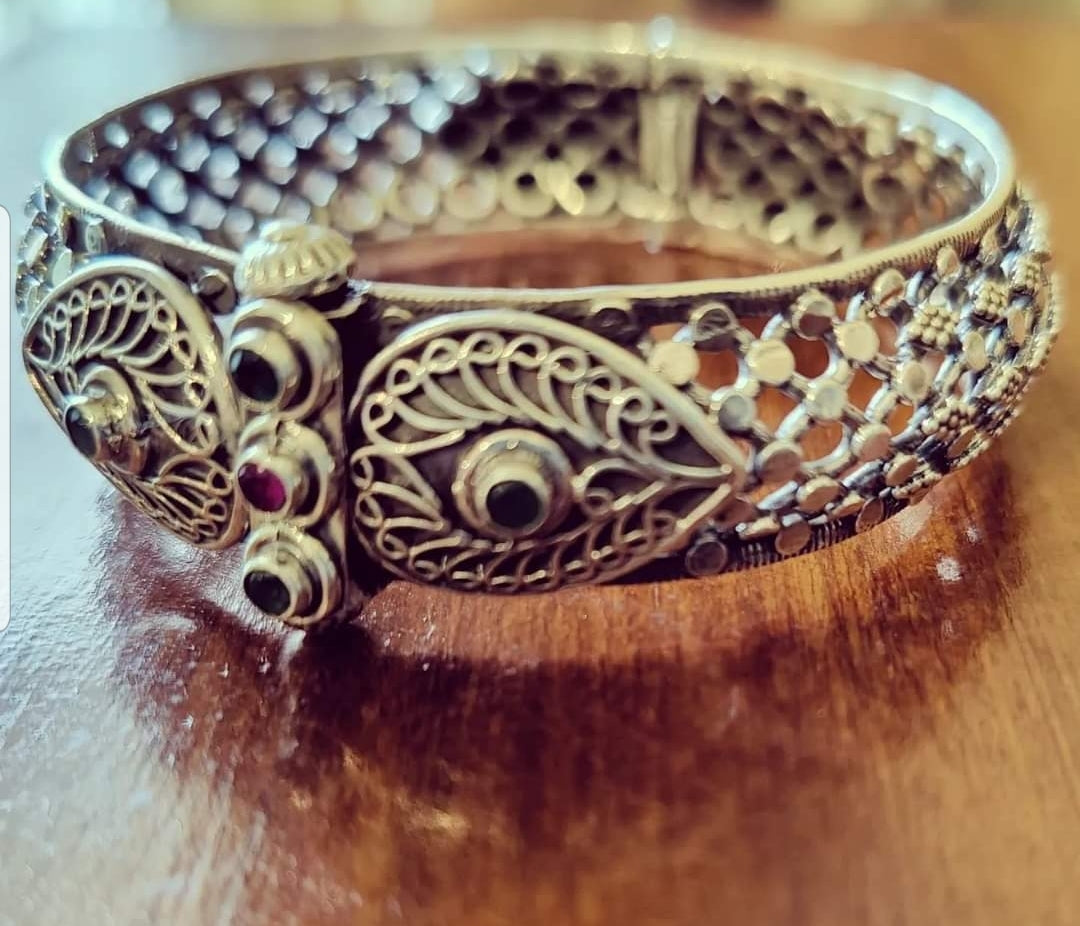 Silver kada (bangle) with intricate jaali (mesh) design enhanced with red and green stone