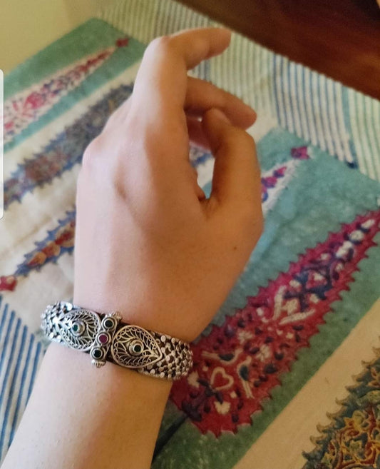 Silver kada (bangle) with intricate jaali (mesh) design enhanced with red and green stone