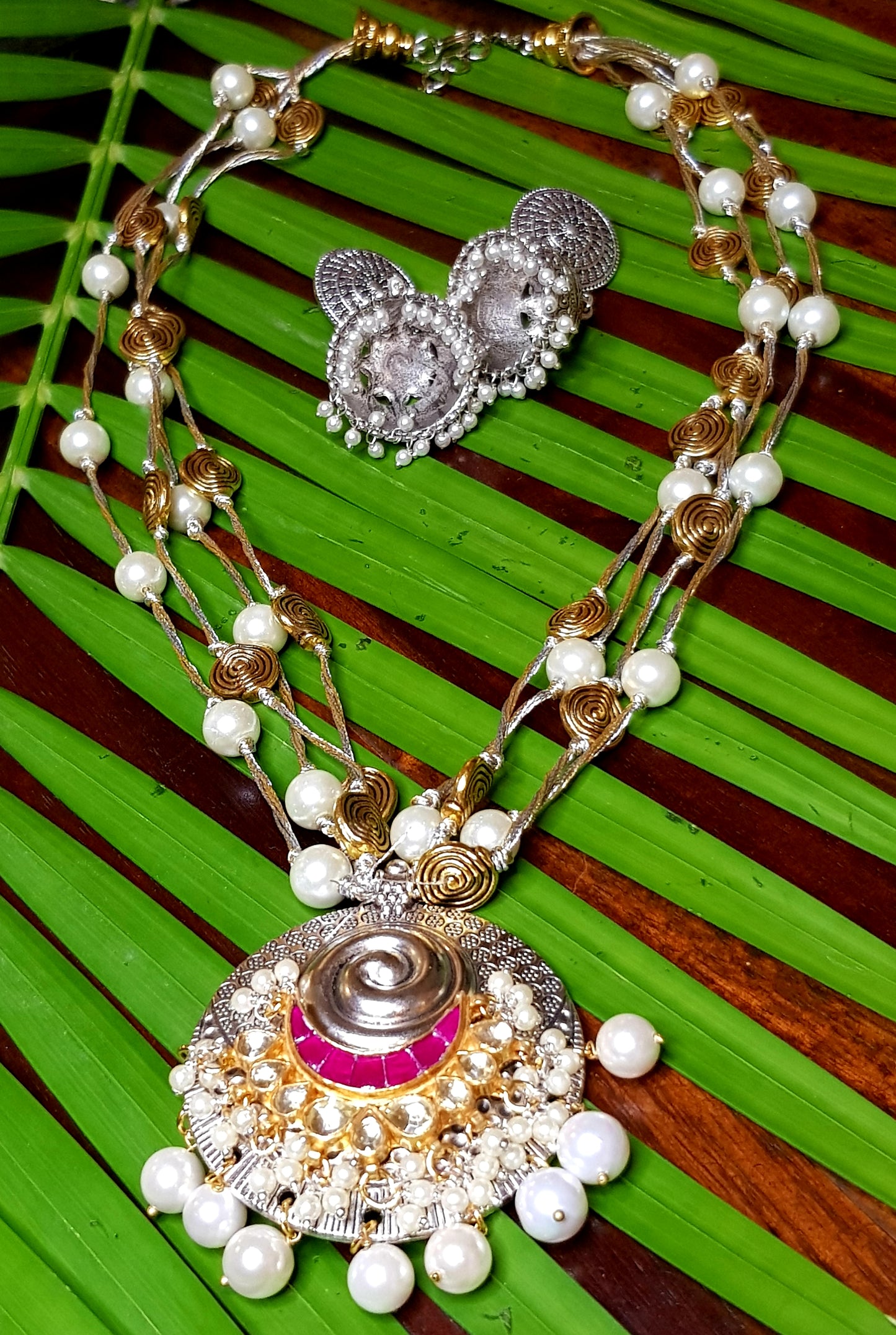 A funky set in silver finish with pearls and golden coils on multiple strings ,a pendant with red/green  stone,kundan and pearls,Big earring/jhumkis