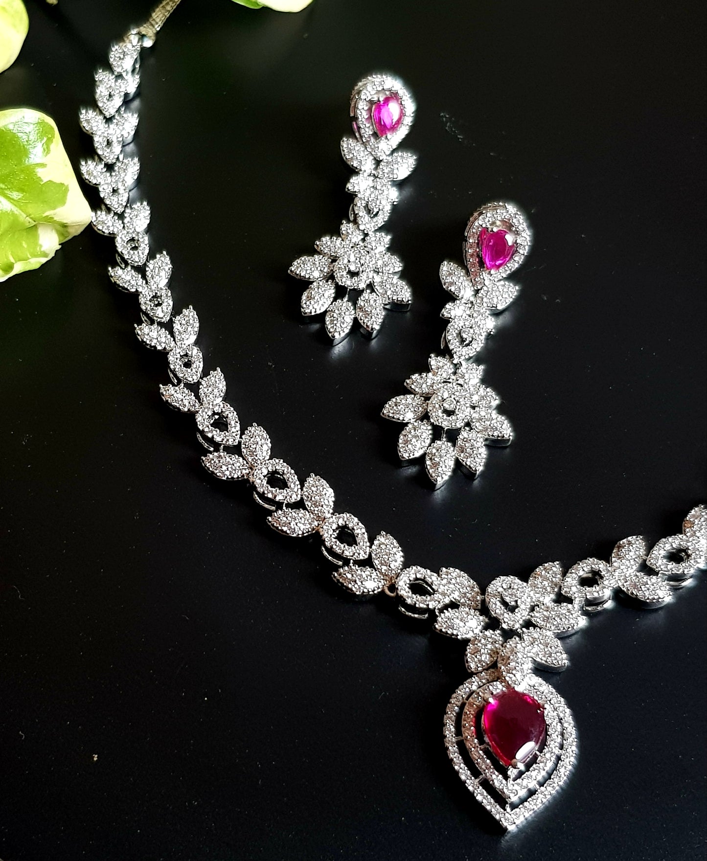 Platinum finish single strand set in leaf inspired CZ design and teardrop shaped ruby/emerald stone pendant, matching earrings