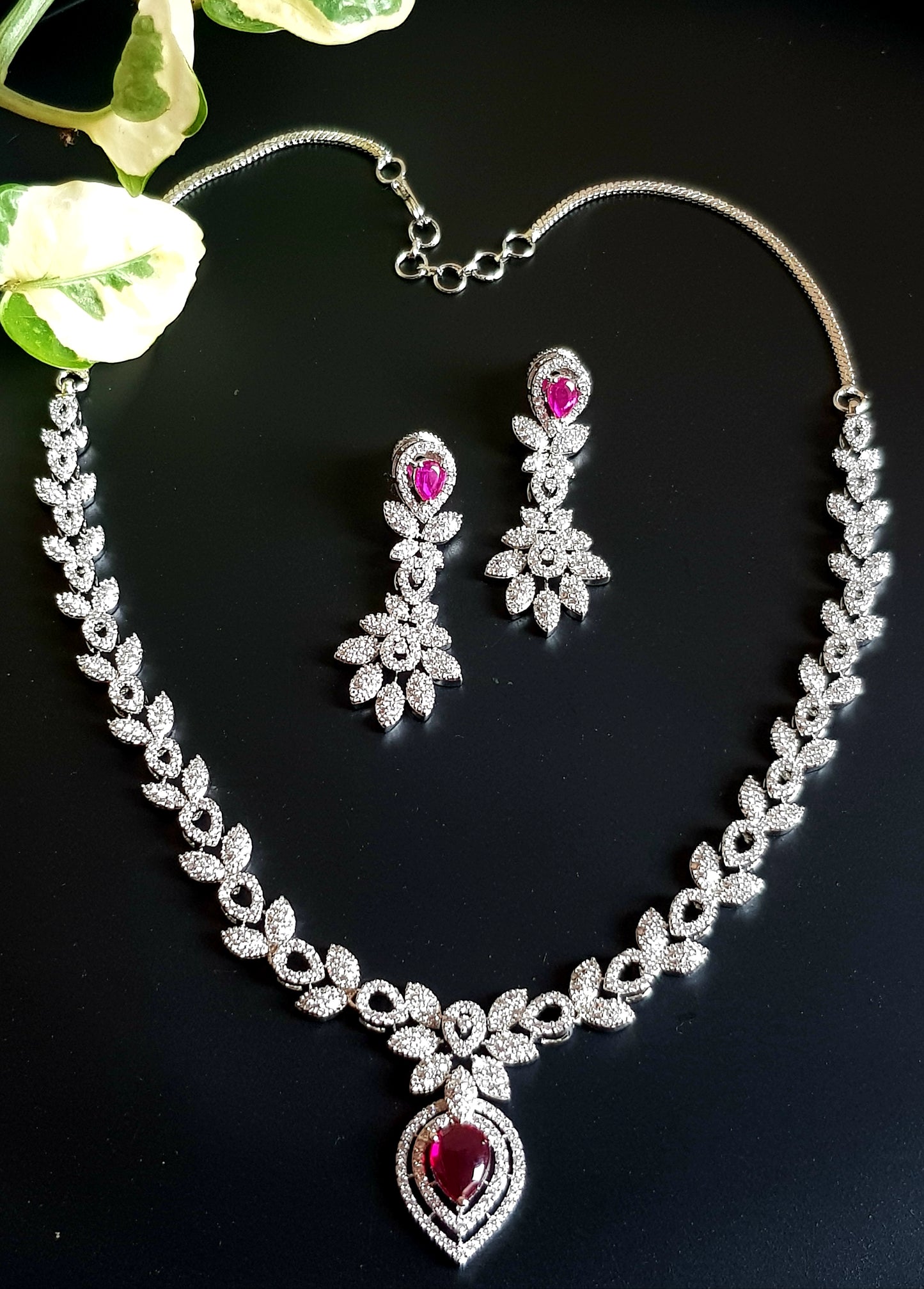 Platinum finish single strand set in leaf inspired CZ design and teardrop shaped ruby/emerald stone pendant, matching earrings